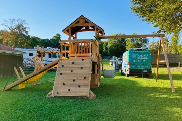 nearly complete wooden playset installation with bear playgrounds van in yard