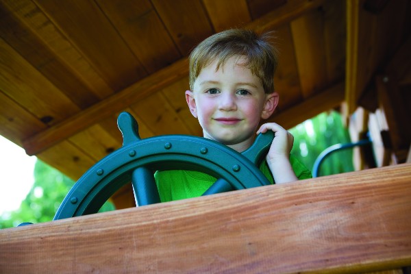 young boy playing with a plastic ships steering wheel mounted in his playset